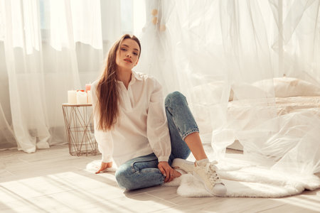 Charming caucasian woman sits in front of bed at light room at homeの写真素材