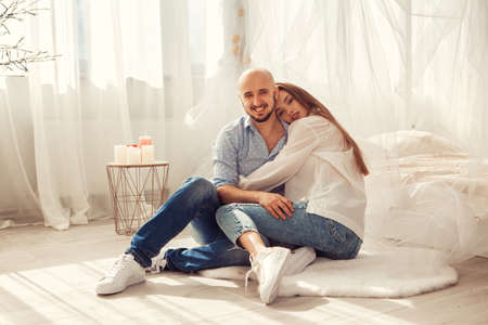 Beautiful couple in love hugs and kisses in white room at homeの写真素材