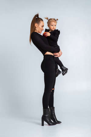 Sexy young mother in black clothes hold her little daughter in hands in studioの写真素材