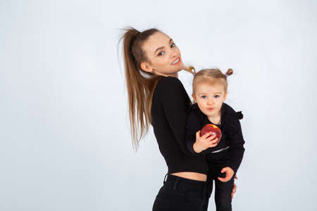 Sexy young mother in black clothes hold her little daughter in hands in studioの写真素材