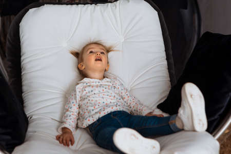 funny little girl sits on white chair and looks aside at homeの写真素材