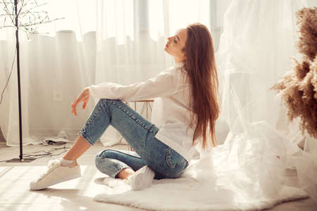 Charming caucasian woman sits in front of bed at light room at homeの写真素材
