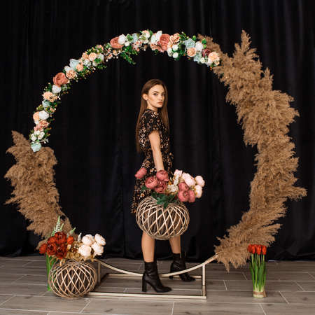 Beautiful woman posing at circle of deadwood in dress with flower print in studioの写真素材