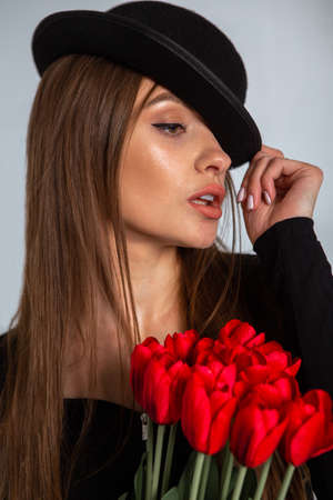 portrait of a beautiful girl in a hat with tulips in hands in studioの写真素材
