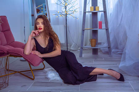 Gorgeous lady in black overall and high heels sits on the hanging glass chair and looks at the cameraの写真素材