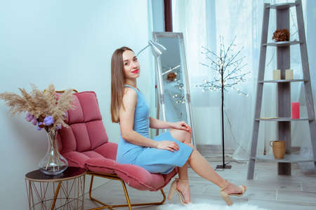 Glamor woman with red lips in black overalls sits on the chair at home and looking at the cameraの写真素材