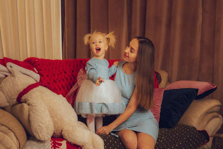 funny mother with her little baby girl sits on the couch at home and screamsの写真素材