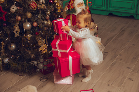 portrait of Cutie little baby girl plays with presents at christmas treeの写真素材
