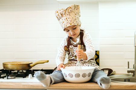 portrait of cute little homecook girl in white kitchen. Happy family kitchen time.