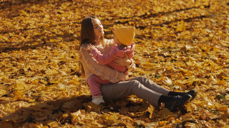 young cute mom and her little daughter at autumn time outdoorsの写真素材