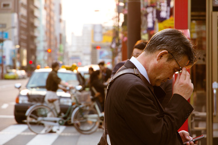 Businessman checks his mobile phone while waiting for a busのeditorial素材