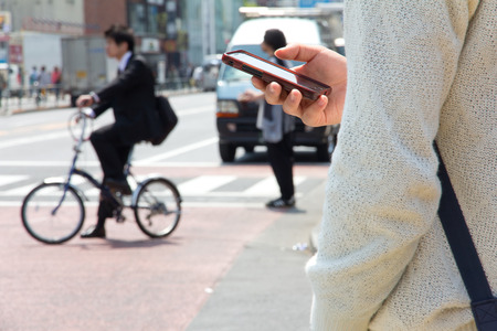 Unidentified Japanese male uses text chat on the phone while walking on the street のeditorial素材