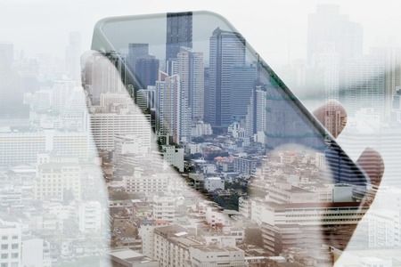 Double exposure image of using smart phone with cityscape background, Communication technology conceptの写真素材