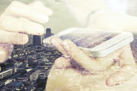 Double exposure of using smart phone and cityscape background ,Business technology concept.の写真素材