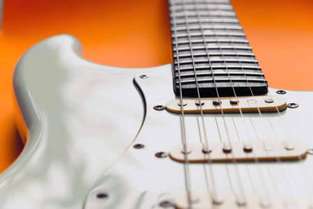 Detail of White Electric Guitar on a orange background.