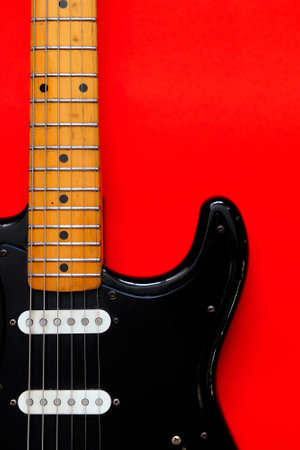 Black electric guitar on a red background. Close-up, copy spaceの写真素材