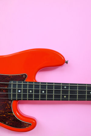 Red electric bass guitar on a pink background. Close-up image.