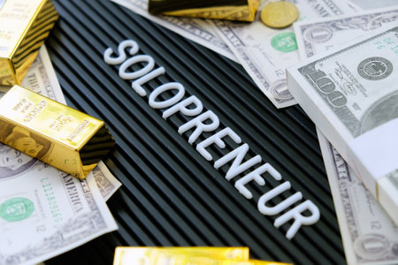 Business concept. Gold bars and dollars on a black background with the word solopreneur.の写真素材