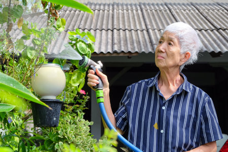 Senior asian woman watering the garden with hose in home garden.の写真素材
