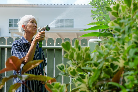 Senior woman watering the garden with hose in home garden.