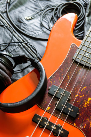 orange electric bass guitar, headphones and cable on a black leather jacket background.