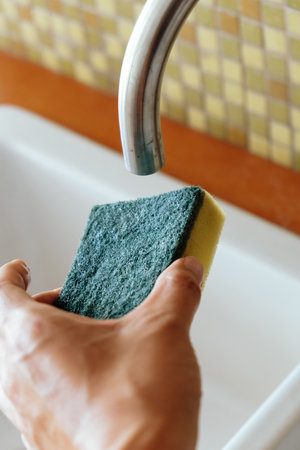 Hand holding sponge in the kitchen sink. Cleaning and washing concept.の写真素材