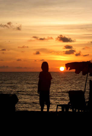 Boy as silhouette in sunset by the oceanの写真素材