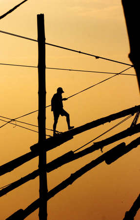 Fisherman walking on a mast in the sunsetの写真素材