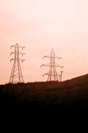 Power poles on a green hill in sunsetの写真素材