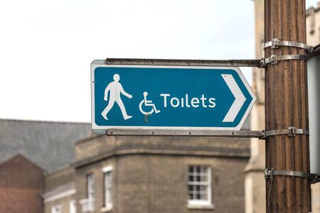 Sign: White Toilet Symbol on Blue Banner with Buildingの写真素材