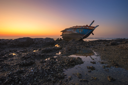 Fishing boat aground on the rocks for a long time at sea erosion disintegrated until only half a body which remains beautiful during twilight.の写真素材