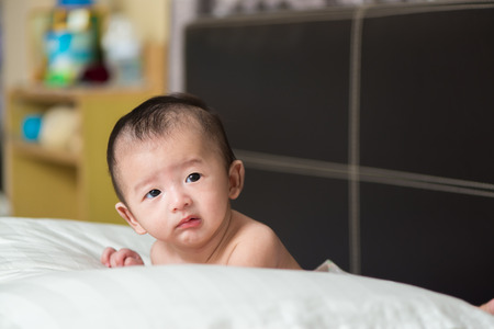 Cute Asian baby about 3 months ages lying, on a white pillow on brown bedの写真素材