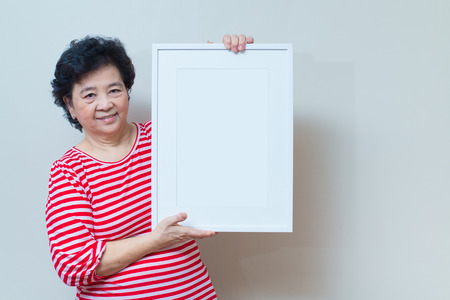 Asian woman showing and holding empty white picture frame in studio shot, specialty tones with soft shadowの写真素材