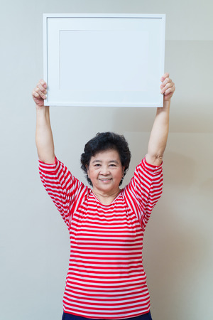 Asian woman showing and holding empty white picture frame in studio shot, specialty tones with soft shadowの写真素材