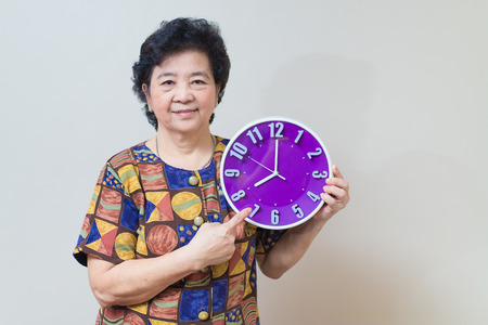Asian senior woman showing and holding purple or violet clock in studio shot, specialty tones with soft shadowの写真素材