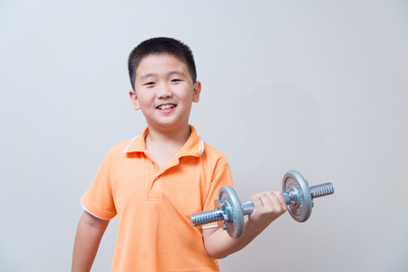 Asian strong boy lifting weights, on grey wall background with soft shadowの写真素材