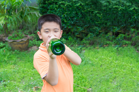 Asian boy drinking water from bottle, in garden, green backgroundの写真素材