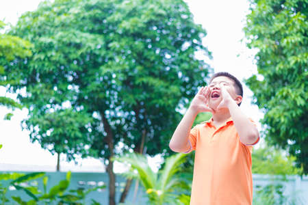 Portrait of Asian child yelling, screaming, shouting, hand on his mouth, in gardenの写真素材