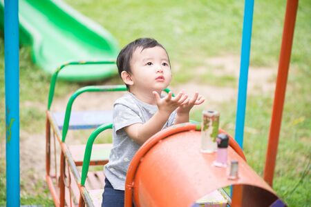 Young Asian boy play a iron train swinging at the playground under the sunlight in summer, Kids play on school yard. Happy kid in kindergarten or preschool. Children having fun at daycare play ground.の写真素材