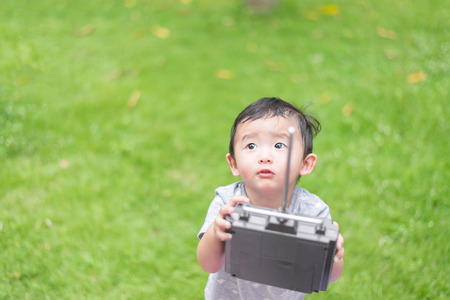 Little Asian kid holding a radio remote control (controlling handset) for helicopter , drone or plane at the playground, school yard. Happy kid in kindergarten or preschool. shallow DOFの写真素材
