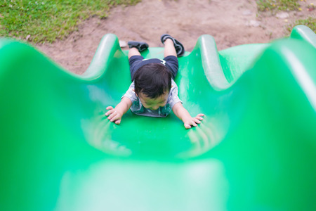 Little Asian kid climbing up the slide at the playground under the sunlight in summer, Kids play on school yard. Happy kid in kindergarten or preschool. shallow DOFの写真素材