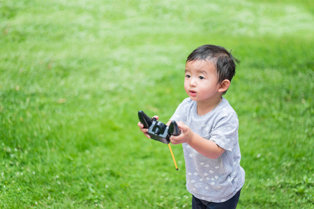 Little Asian kid holding a radio remote control (controlling handset) for helicopter , drone or plane at the playground, school yard. Happy kid in kindergarten or preschool.の写真素材