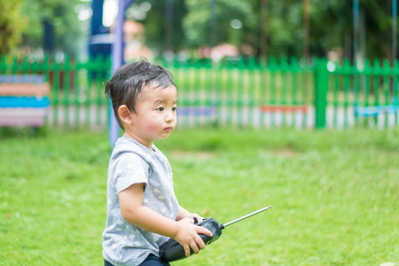 Little Asian kid holding a radio remote control (controlling handset) for helicopter , drone or plane at the playground, school yard. Happy kid in kindergarten or preschool.shallow DOFの写真素材
