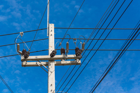 High voltage power pole with wires tangled on blue sky background.