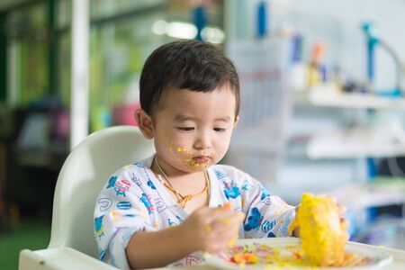 Asian kid eating birthday cake with cream on face at home. shallow DOF.の写真素材