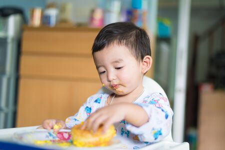 Asian kid eating birthday cake with cream on face at home. shallow DOF.の写真素材