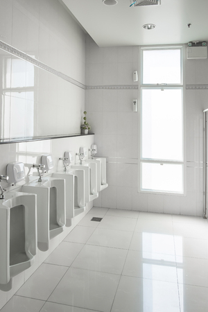 White urinals in clean men public toilet room empty with big window and light from outside, interior.の写真素材