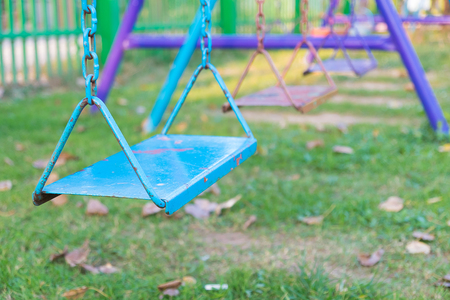 Empty chain and metal swings in playground and meadow grass field under sun light in summer.の写真素材