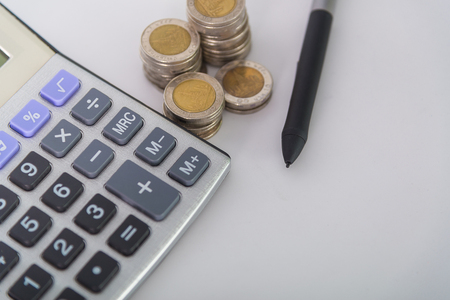 Savings, increasing columns of coins, piles of coins arranged as a graph and calculator with pen on white background, business idea, shallow focus.の写真素材