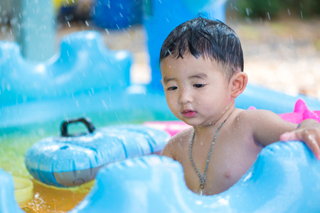 Asian kid playing in inflatable baby pool. Boy swim and splash in colorful swimming pool with water toys on hot summer day. shallow focusの写真素材